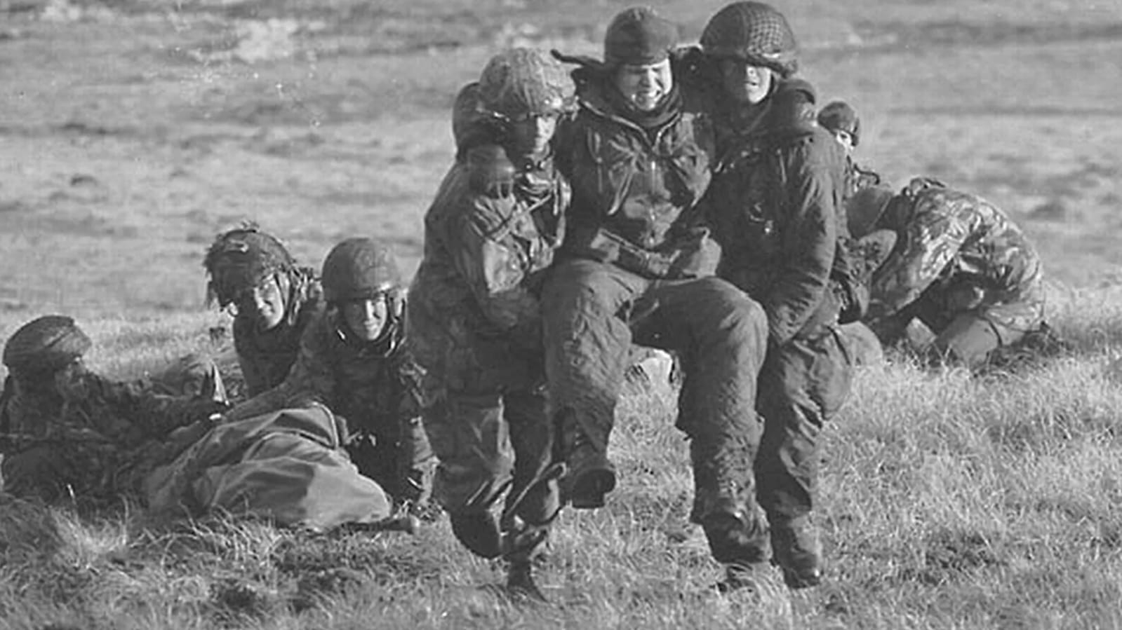 Soldados argentinos evacuando o auxiliando a un compañero herido en el campo durante la Guerra de Malvinas, fotografía en blanco y negro.