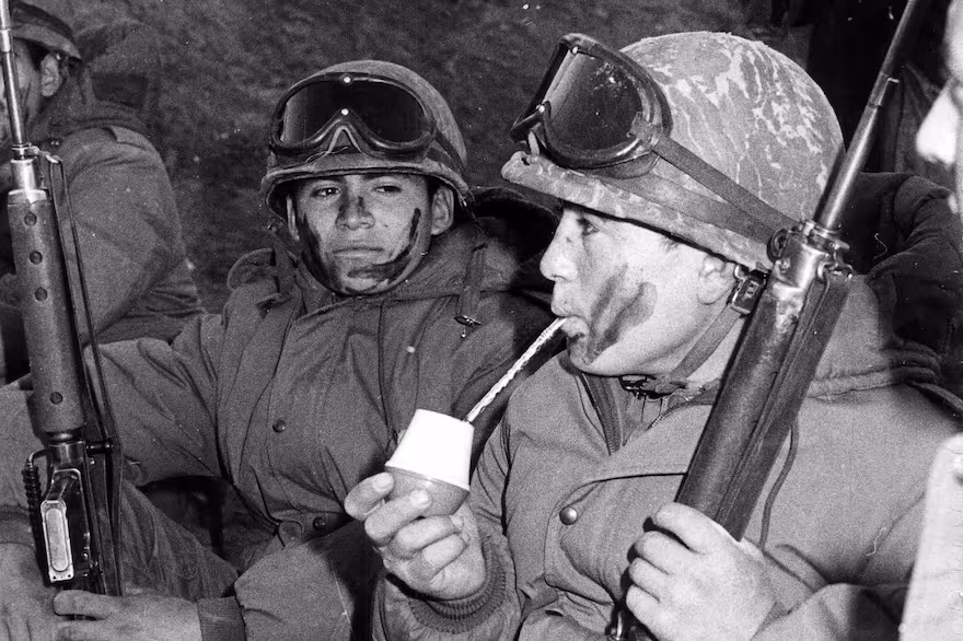 Soldado argentino en uniforme tomando mate en el exterior, gesto cotidiano de la cultura nacional en medio del conflicto.